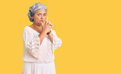 Senior woman with gray hair wearing bohemian style holding symbolic gun with hand gesture, playing killing shooting weapons, angry face