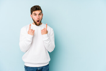 Young caucasian man isolated on blue background pointing upside with opened mouth.