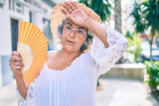 Middle age woman with grey hair using handfan on a very hot day of a heat wave