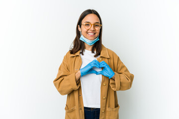 Young latin woman wearing a mask to protect from covid isolated on white background smiling and showing a heart shape with hands.