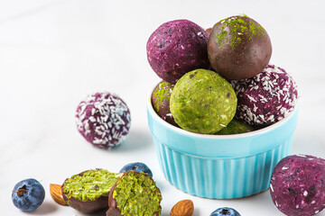 Raw energy balls with acai berry powder and matcha tea in chocolate glaze on white table. Healthy...
