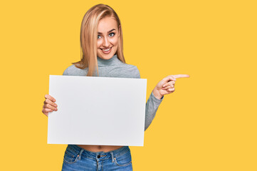 Beautiful caucasian woman holding blank empty banner smiling happy pointing with hand and finger to the side