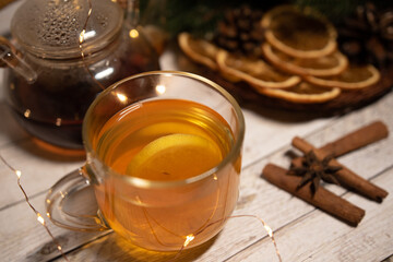 
a cup of hot Christmas tea with lemon on a light wood. against the background of an asterisk star anise, an orange and a sprig of a Christmas tree. christmas concept