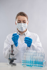 Close-up view of female microbiologist in biohazard protective clothing explore with microscope biological tube with vaccine. White background.