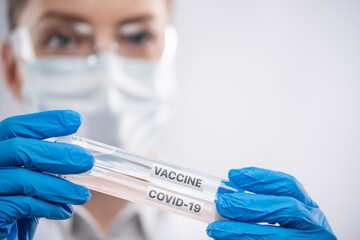 Close-up view of female microbiologist in biohazard protective clothing looking for biological tubes with vaccine and covid-19 sample. Research and development concept.