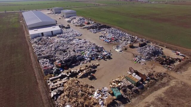 Large Recycling Site Adjacent To Circulated Road. Piles Of Rubber Tires, Plastics, Foils, Metals, Wood Pallets. Claw Crane Loader, Forklift And Trash Compactor Visible.