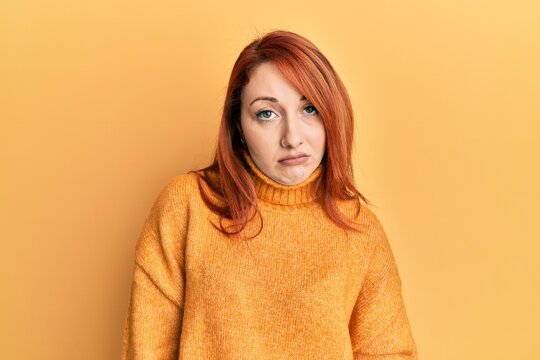 Beautiful redhead woman wearing casual winter sweater over yellow background looking sleepy and tired, exhausted for fatigue and hangover, lazy eyes in the morning.