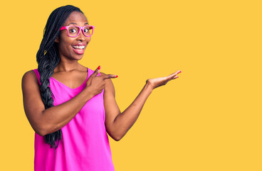 Young african american woman wearing casual clothes and glasses amazed and smiling to the camera while presenting with hand and pointing with finger.