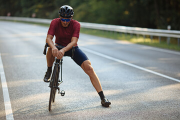 Fototapeta na wymiar Muscular cyclist relaxing on road during riding