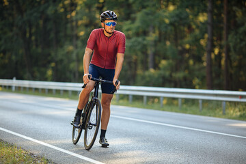Fototapeta na wymiar Sportsman in helmet standing on paved road with bike