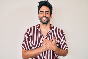 Handsome hispanic man with beard wearing casual clothes smiling with hands on chest with closed eyes and grateful gesture on face. health concept.