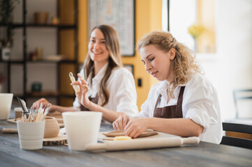 Female potters during the working process in the clay workshop. Woman masters prepare ceramic and clay products at big wooden table