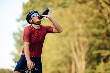 Fototapeta premium Exhausted road cyclist drinking water from bottle