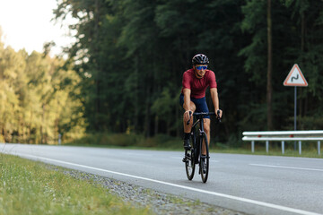 Fototapeta na wymiar Young athlete in helmet riding bike on paved road