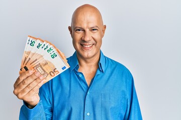 Middle age bald man holding 50 euro banknotes looking positive and happy standing and smiling with...
