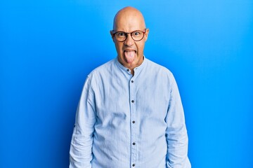 Middle age bald man wearing casual clothes and glasses sticking tongue out happy with funny expression. emotion concept.