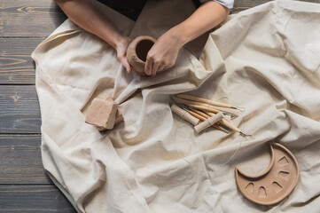 A young potter woman making pot in her own working place. Standing in spacious studio creating the...