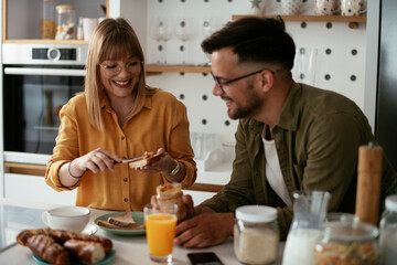 Young couple making sandwich at home. Loving couple drinking coffee while preparing the breakfast.