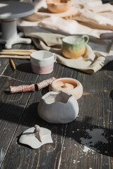 A close-up view of clay plates and a paint brush on a wooden table and dried flowers on a background. Crafted tableware in a pottery studio. Handmade ceramic. Pottery studio concept.