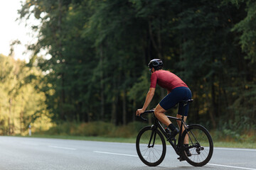 Fototapeta premium Back view of muscular guy in helmet riding bike on road