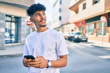 Young arab man smiling happy using smartphone walking at city.