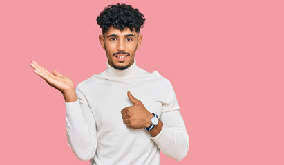 Young arab man wearing casual winter sweater showing palm hand and doing ok gesture with thumbs up, smiling happy and cheerful