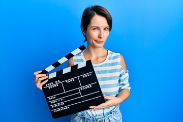 Young brunette woman with short hair holding video film clapboard skeptic and nervous, frowning...