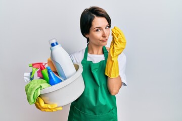 Young brunette woman with short hair wearing apron holding cleaning products doing italian gesture with hand and fingers confident expression