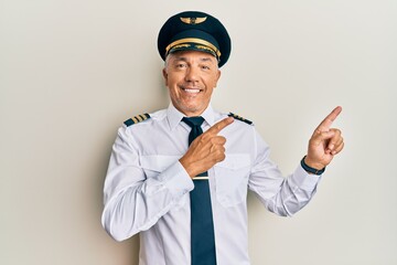 Handsome middle age mature man wearing airplane pilot uniform smiling and looking at the camera pointing with two hands and fingers to the side.