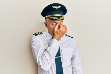 Handsome middle age mature man wearing airplane pilot uniform tired rubbing nose and eyes feeling...