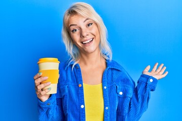 Young blonde girl holding take away coffee celebrating achievement with happy smile and winner...