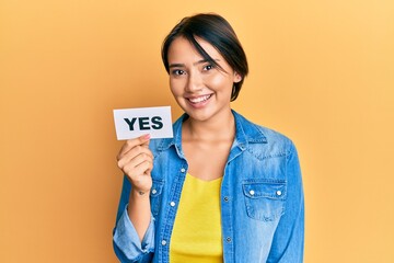 Beautiful young woman with short hair holding yes reminder looking positive and happy standing and...
