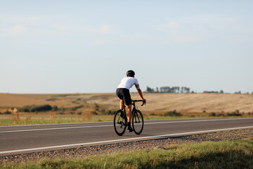 Fototapeta na wymiar Back view of young man in helmet riding bike on road
