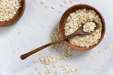 Whole oat flakes in wooden bowls on a light cement background, tinted