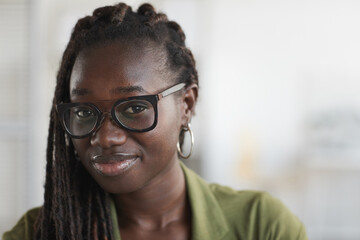 Close up portrait of stylish young African woman wearing glasses and smiling at camera against...
