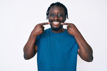 Fototapeta premium Young african american man with braids wearing casual clothes smiling cheerful showing and pointing with fingers teeth and mouth. dental health concept.