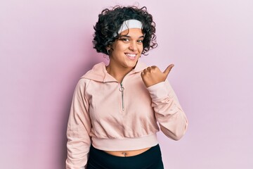 Hispanic woman with curly hair wearing sportswear looking confident with smile on face, pointing oneself with fingers proud and happy.