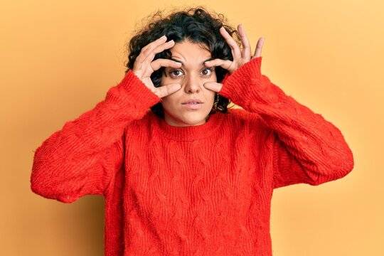 Hispanic woman with curly hair wearing casual winter sweater crazy and mad shouting and yelling with aggressive expression and arms raised. frustration concept.