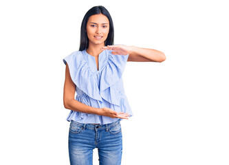 Fototapeta premium Young beautiful latin girl wearing casual clothes gesturing with hands showing big and large size sign, measure symbol. smiling looking at the camera. measuring concept.