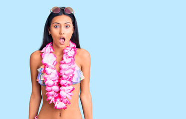 Young beautiful latin girl wearing bikini and hawaiian lei scared and amazed with open mouth for surprise, disbelief face