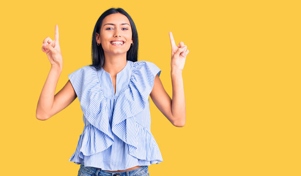 Young beautiful latin girl wearing casual clothes smiling amazed and surprised and pointing up with fingers and raised arms.