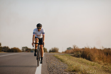 Muscular guy in helmet and glasses riding bike on road