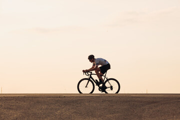 Muscular athlete in helmet cycling on asphalt road