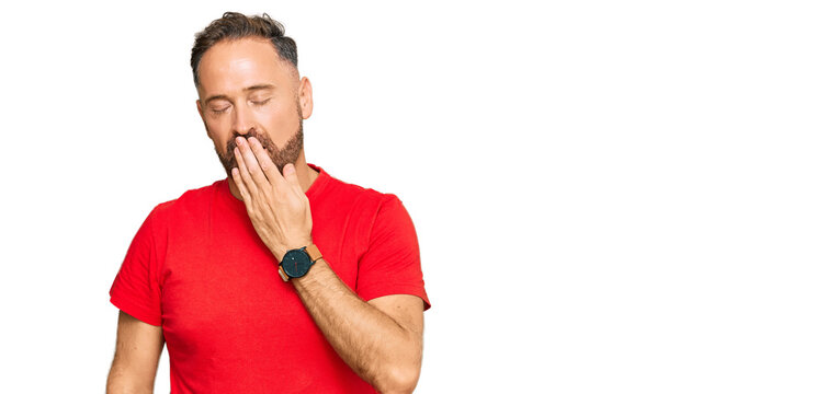 Handsome middle age man wearing casual red tshirt bored yawning tired covering mouth with hand. restless and sleepiness.