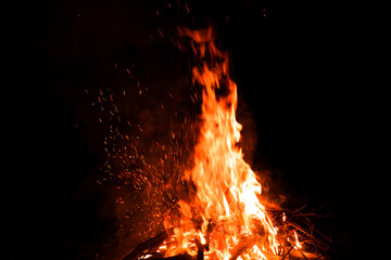 Burning red hot sparks rise from large fire in the night. Fire flames sparks background. Abstract dark glitter fire particles lights.