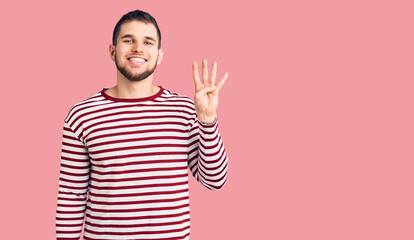 Fototapeta premium Young handsome man wearing striped sweater showing and pointing up with fingers number four while smiling confident and happy.