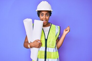 Young african american woman with braids wearing safety helmet holding blueprints screaming proud, celebrating victory and success very excited with raised arms