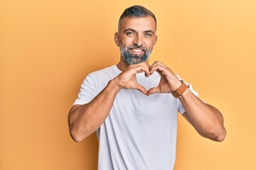 Middle age handsome man wearing casual white tshirt smiling in love doing heart symbol shape with hands. romantic concept.