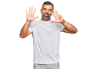 Middle age handsome man wearing casual white tshirt showing and pointing up with fingers number nine while smiling confident and happy.