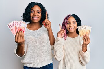 Beautiful african american mother and daughter holding norwegian krone banknotes smiling with an...
